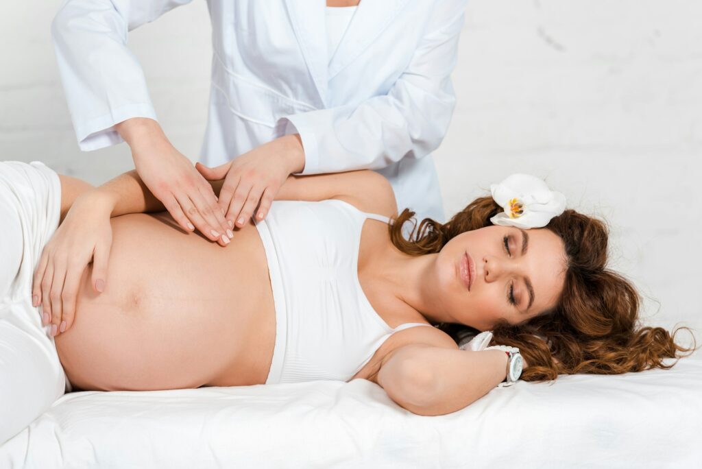 Masseur doing belly massage to pregnant woman with orchid in hair in spa center
