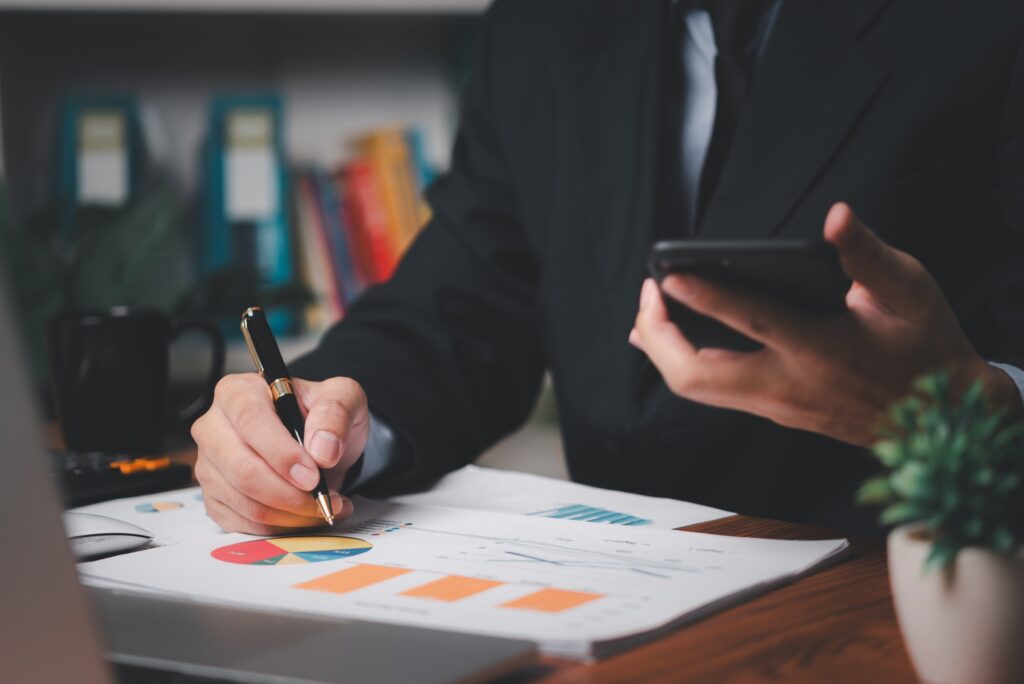 Business men hand holding mobile phones and pens on the desk. business analyzing documents graphs